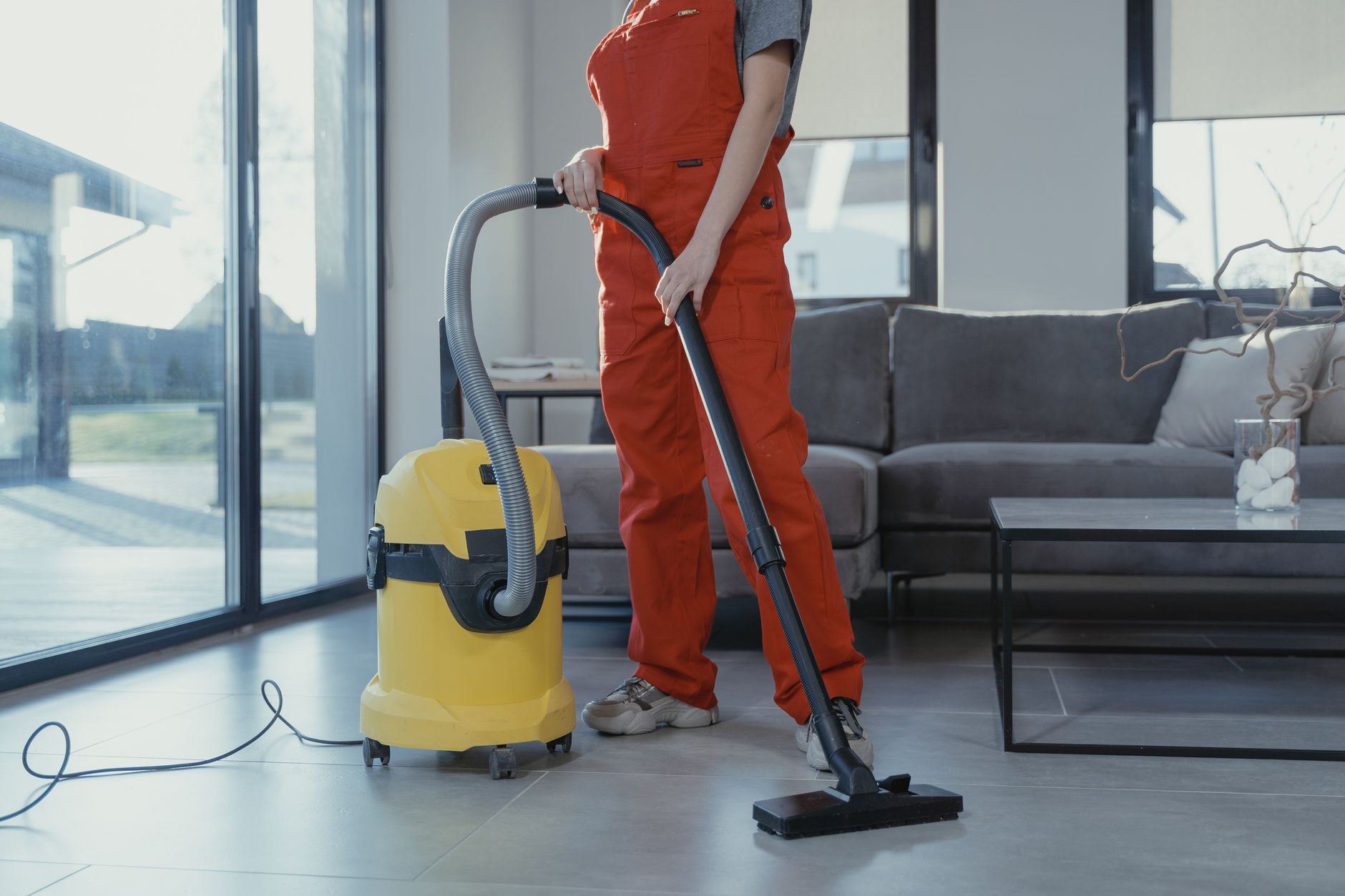 intervenante en salopette rouge passant l'aspirateur dans un salon lumineux