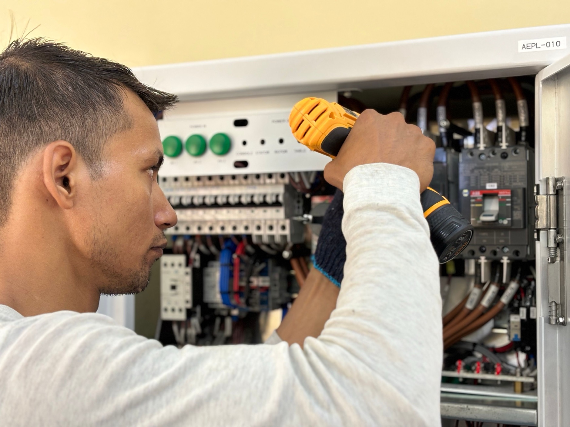 électricien vérifiant un tableau électrique avec une perceuse, câbles et disjoncteurs visibles