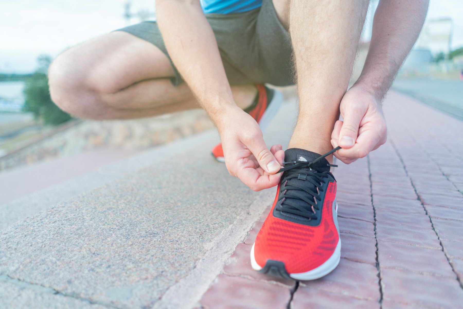 personne en train de lacer une chaussure de running rouge et noire, gros plan sur les mains et la chaussure