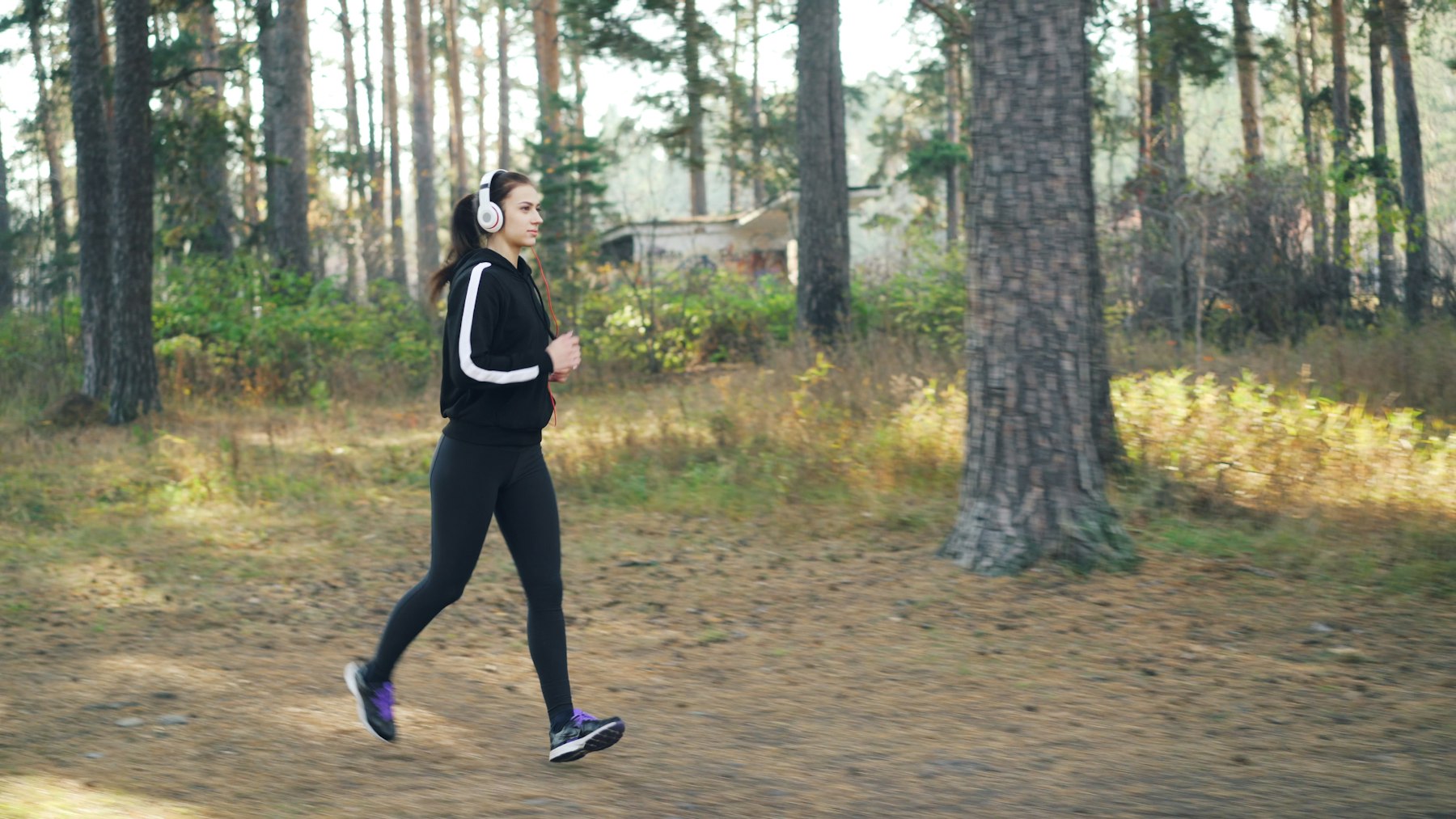 coureuse en tenue technique complète (veste, collant, chaussures de running) qui court sur un chemin en forêt